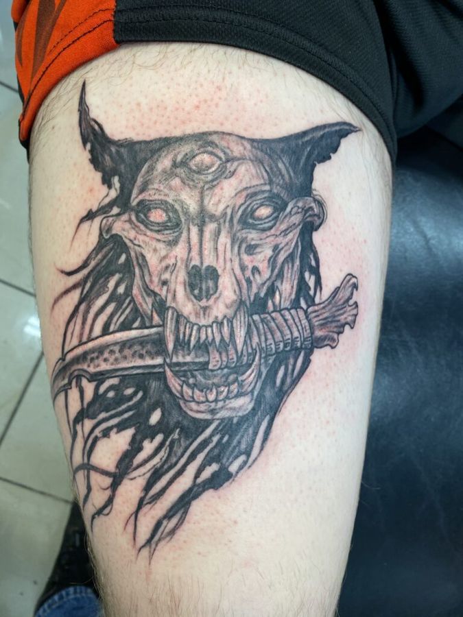 Black and grey wolf skull with dagger on an upper arm, by Steve